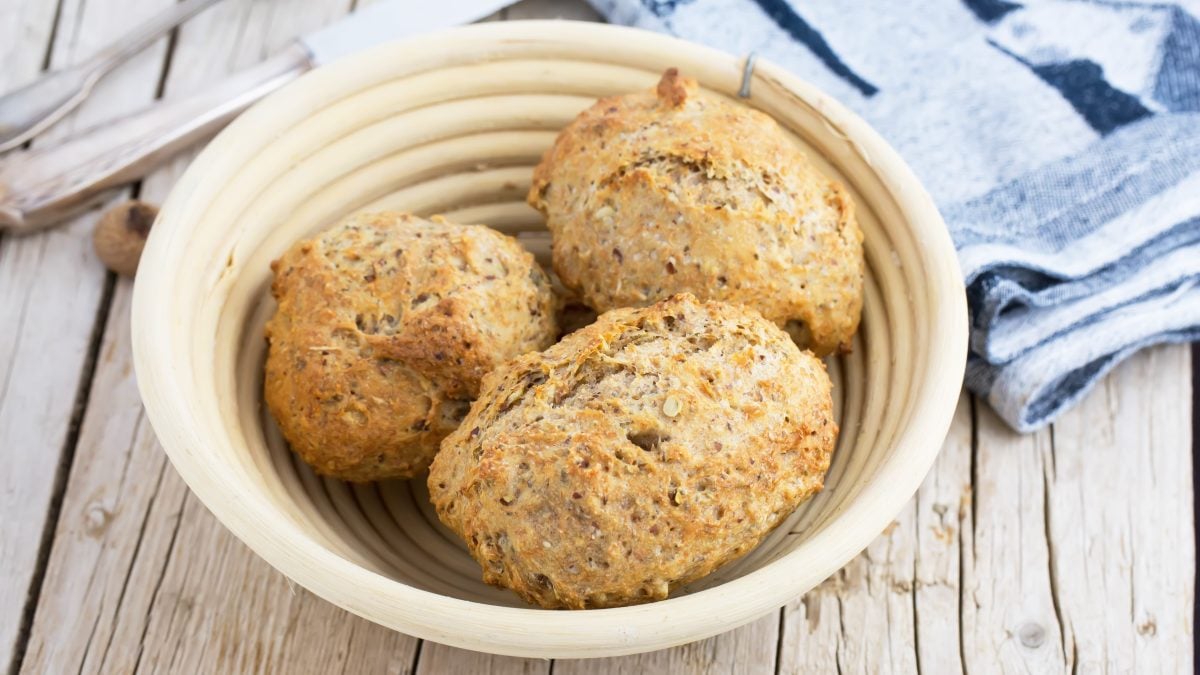 Ein heller Korb mit drei Haferflocken-Brötchen von schräg oben fotografiert.