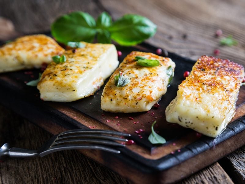 Knusprig gebratener Halloumi mit Kräutern, angerichtet auf einem dunklen Brett vor rustikalem Holztisch.