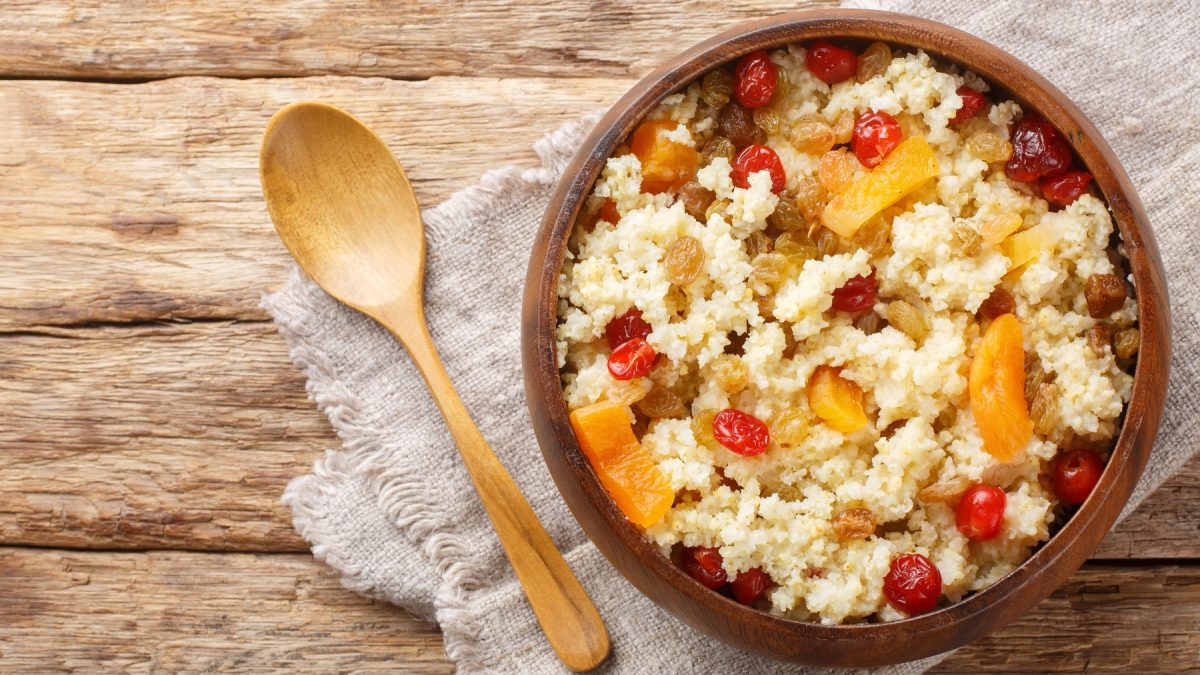 Hirse-Porridge mit getrockneten Aprikosen, Kirschen und Sultaninen in einer Holzschüssel.