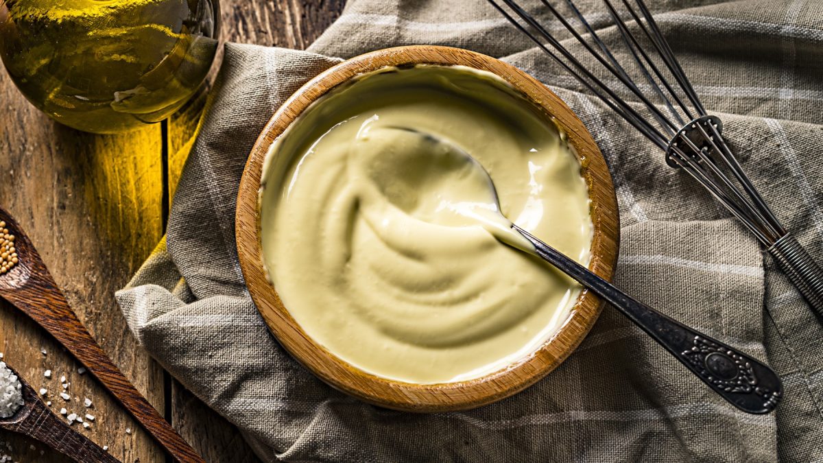 Keqpie Mayo in einem hölzernen Schälchen auf einem dunkelgrauen Geschirrtuch. Rechts ein Schneebesen und in der Schüssel ein Löffel.