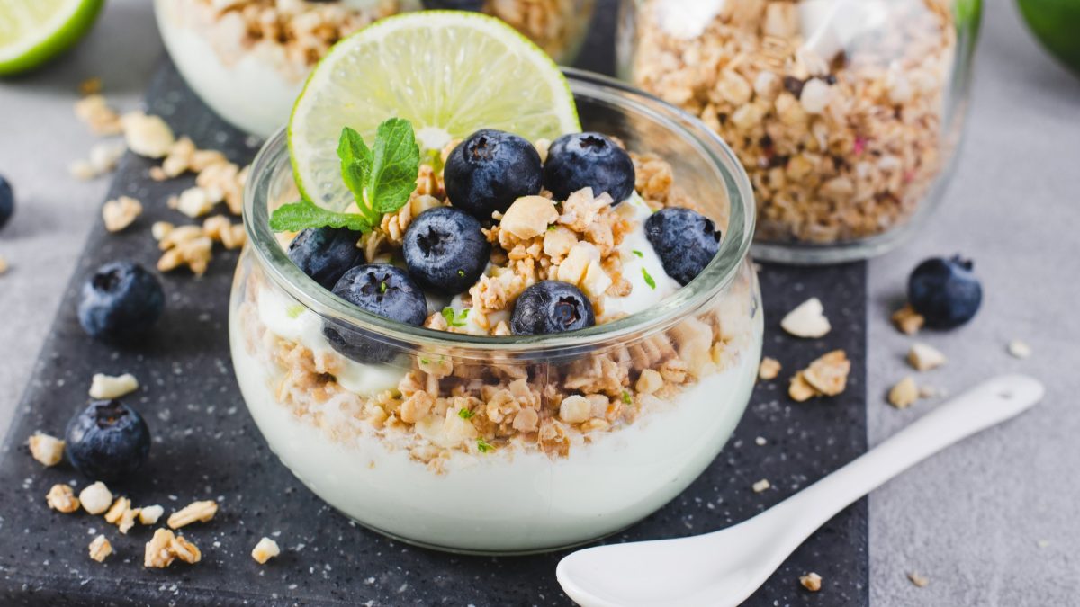 Joghurtparfait im Glass getoppt mit Granola, Blaubeeren, Limettenscheibe und Limettenzeste.