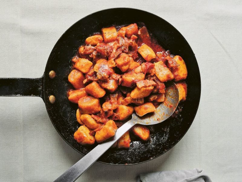 Eine schwarze gusseiserne Pfanne mit den Gnocchi auf einem Tisch mit weißem Stofftuch.