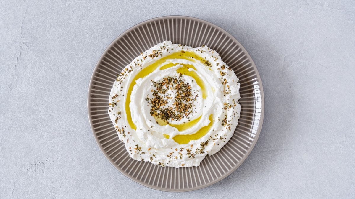 Veganer Labneh auf einem grauen Teller mit Olivenöl und Gewürzen.