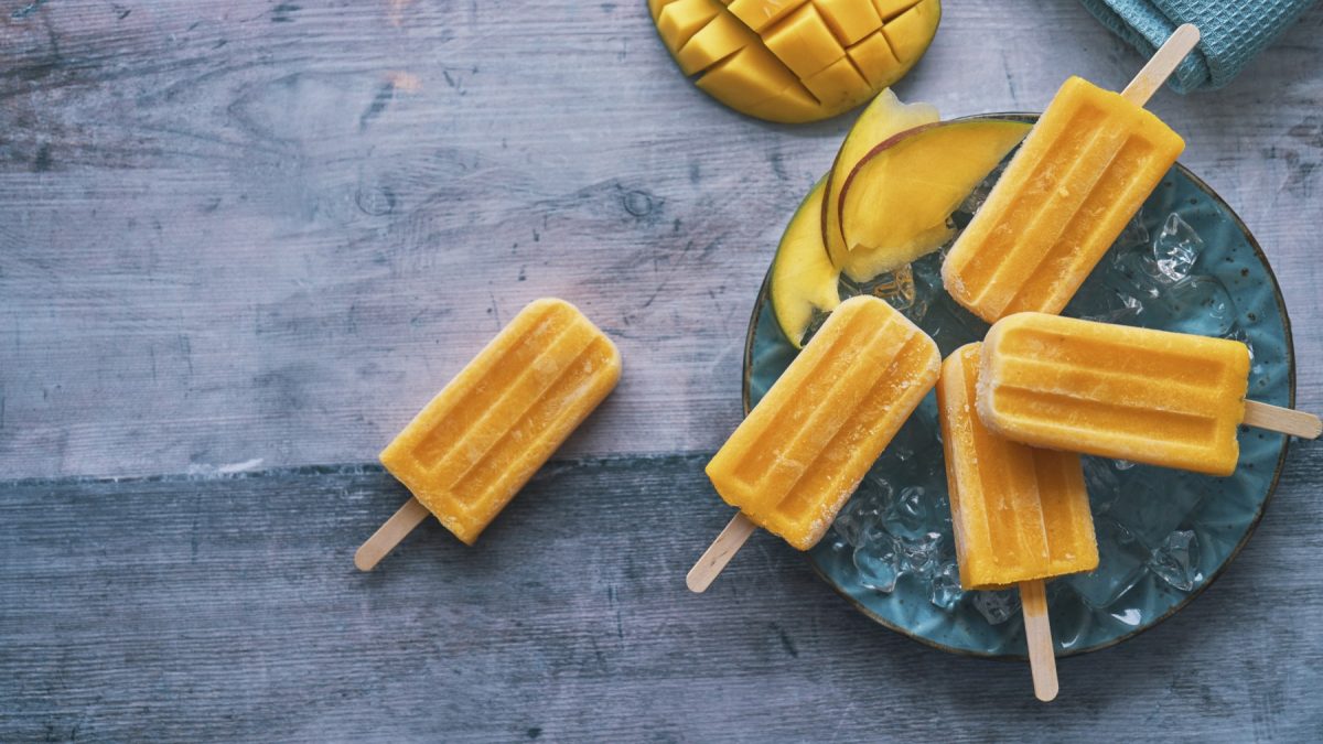 Mango-Lassi-Eis auf einem blauen Teller auf grauem Hintergrund. Oben auf dem Foto eine halbe Mango