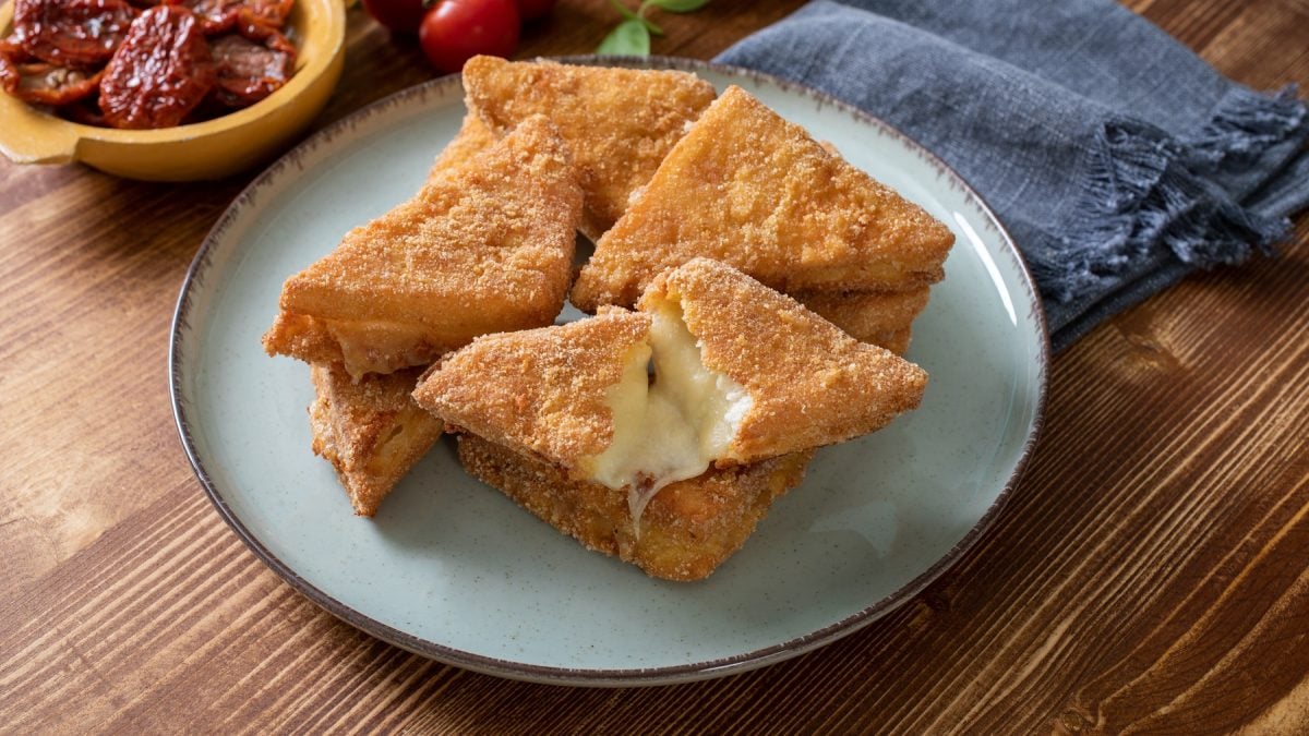 Mozzarella in carrozza auf einem blauen Teller vor einem hölzernen Untergrund.