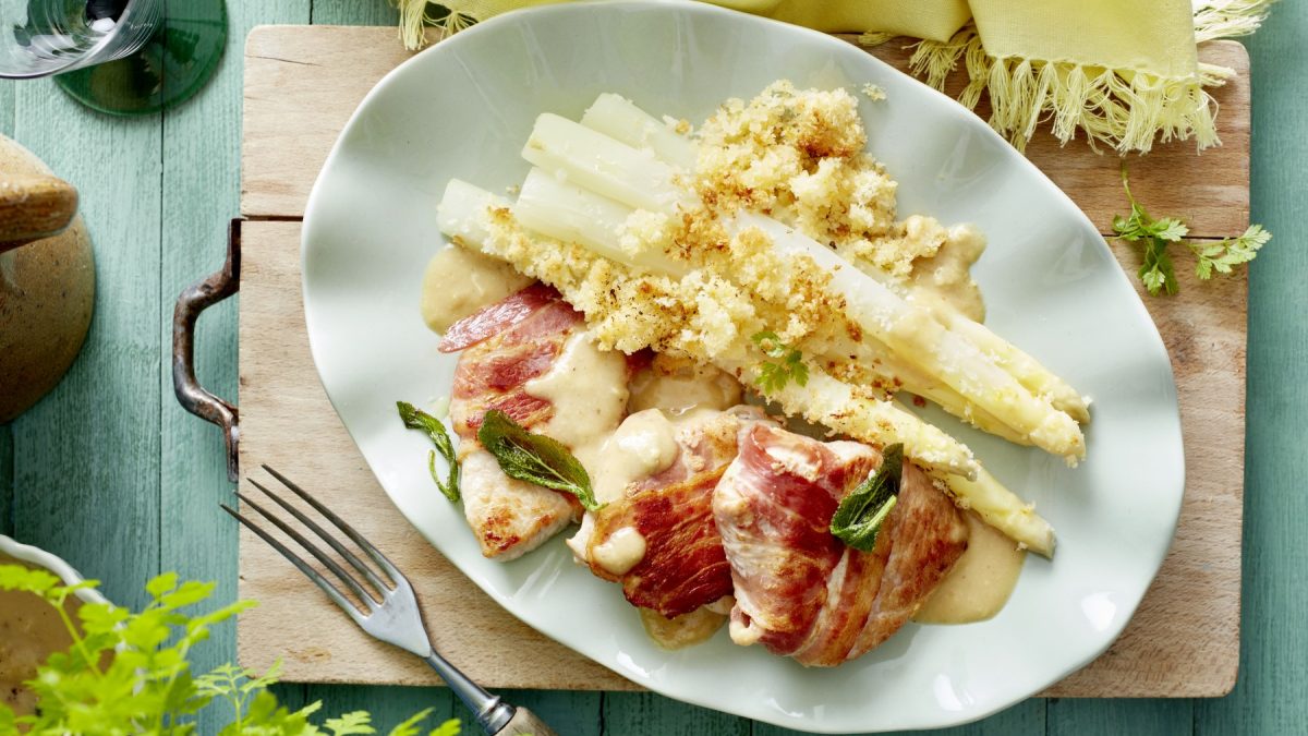 Ofen-Spargel mit Speck-Schnitzel auf weißem Teller mit Holzuntergrund.