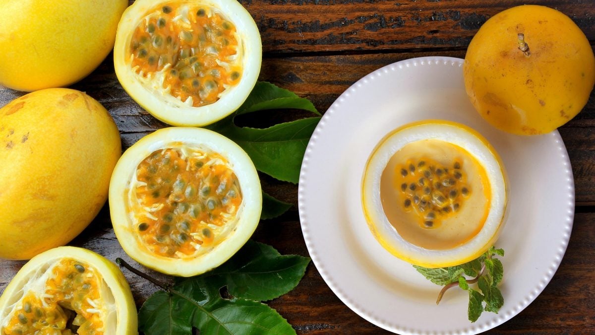 Passionsfrucht-Posset in einer halben Passionsfrucht auf einem Teller, daneben ganze gelbe Passionsfrüchte.