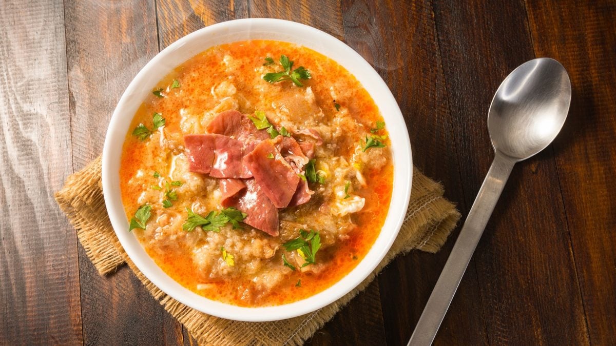 Sopa de ajo in einer weißen Schüssel vor Holzuntergrund von oben fotografiert.