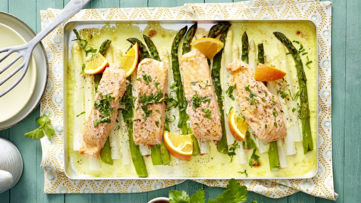 Draufsicht: Spargel-Lachs vom Blech, daneben Pfannenwender, heller Untergrund.