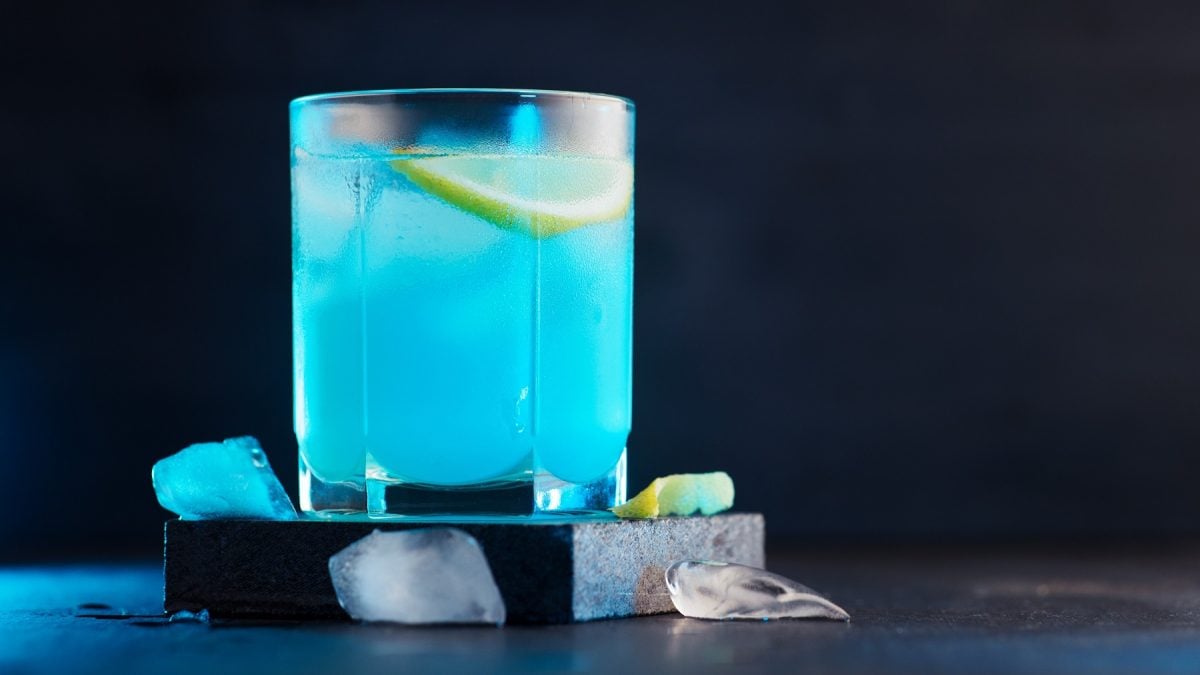 Ein Glas mit dem türkis-blauen Cocktail auf dunklem Untergrund und schwarzem Hintergrund.