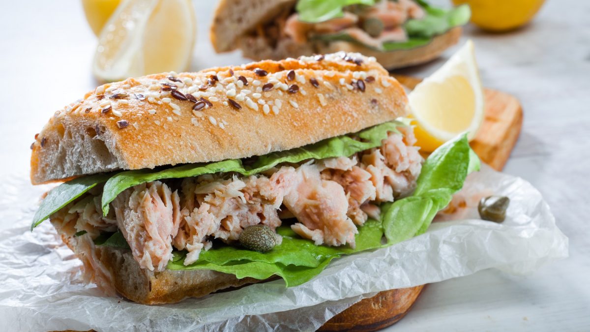 Ein Baguette mit Thunfischsalat belegt auf weißem Pergamentpapier. Alles von der Seite fotografiert.