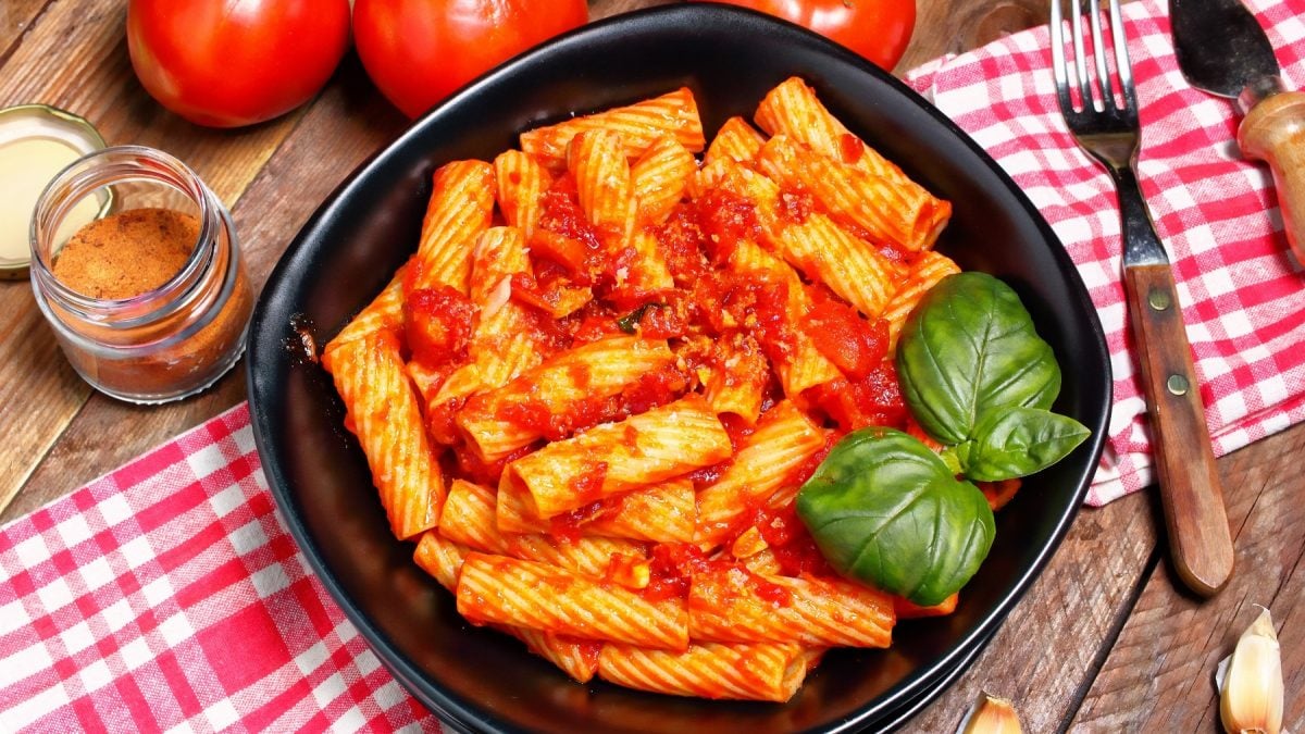 Totiglioni mit Tomatensauce mit Thunfisch mit Basilikumblättern auf einem schwarzen Teller auf einer karierten Tischdecke.