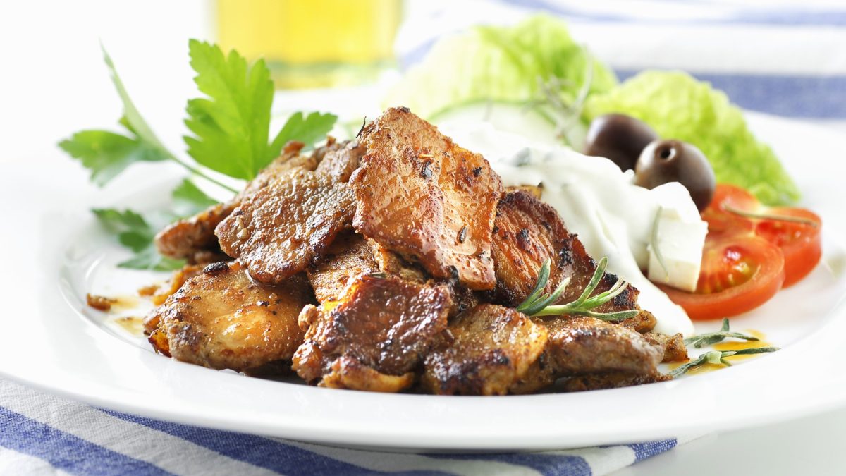 Gyros mit Tsatziki und Salat auf einem weißen Teller.