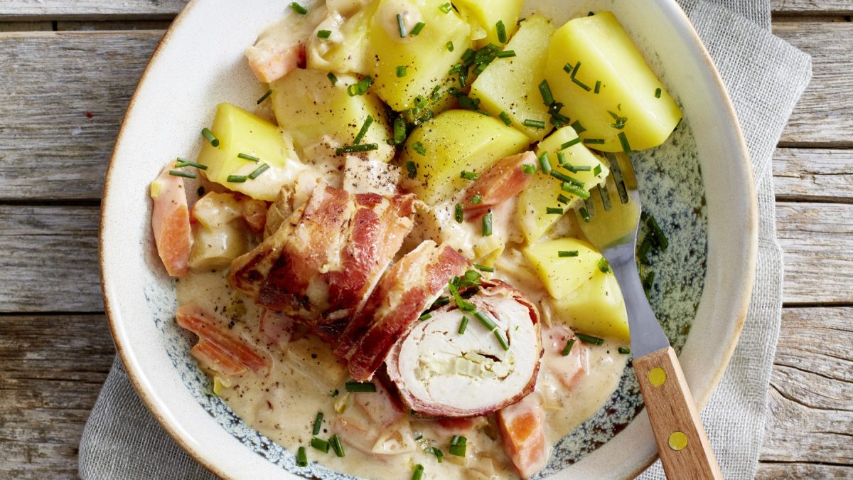 Bacon-Haehnchenroulade auf einem weißen Teller auf hölzernem Hintergrund.