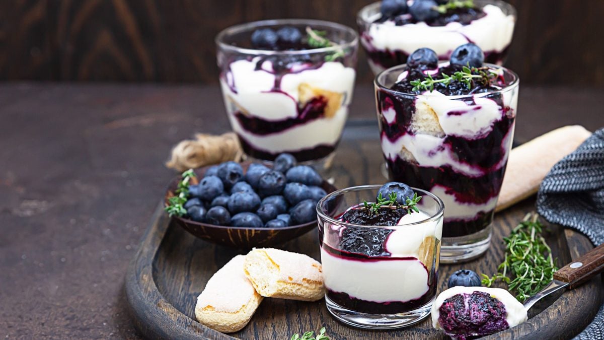 Vier Blaubeer-Mascarpone-Trifle in Gläser vor dunklem Hintergrund.