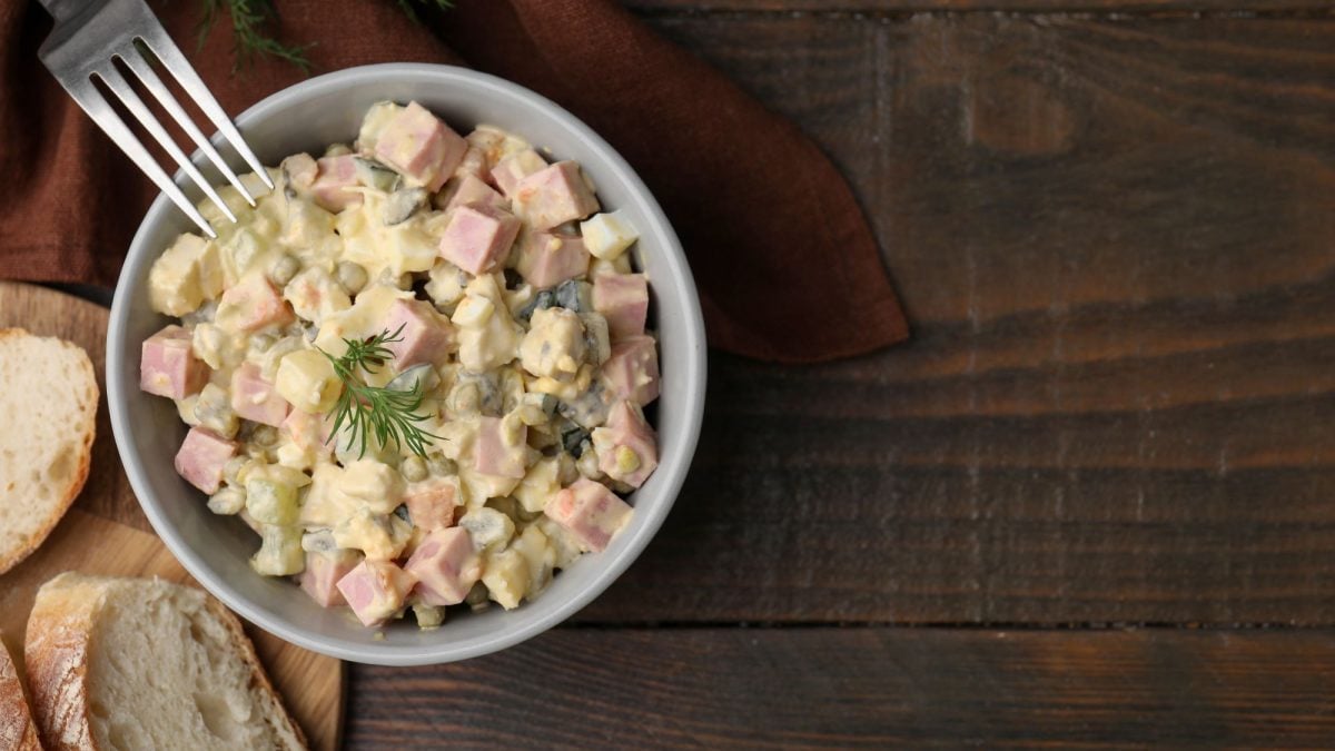 Ein Schälchen mit böhmischen Kartoffelsalat, garniert mit Dill, daneben zwei Scheiben knuspriges Weißbrot auf einem Holztisch.