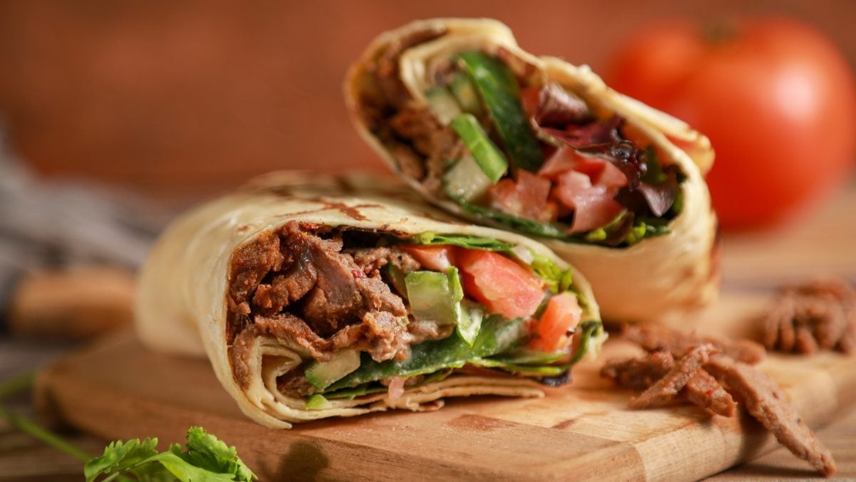 Ein Holzschneidebrett mit dem angeschnittenen Döner-Wrap von der Seite und recht nah fotografiert.