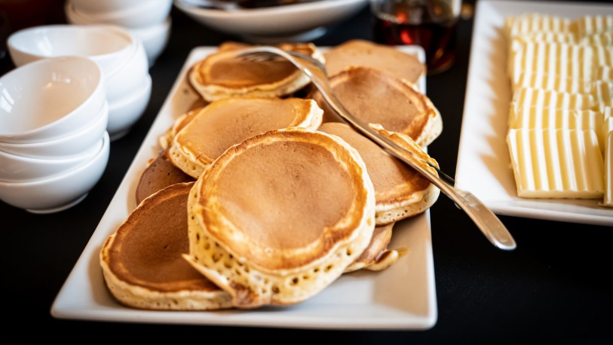 Draufsicht, schräg: eine weiße Platte mit Buchweizen-Quark-Pancakes. Daneben liegen edle weiße leere Schalen. soowie dünne scheiben Knäckebrot.