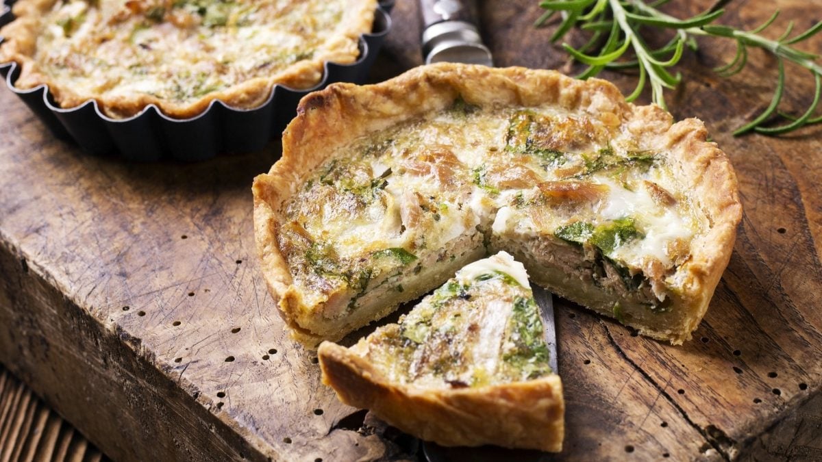 Draufsicht: Zwei Mini-Quiche mit Thunfisch liegen auf einem rustikalen Untergrund aus Holz. Daneben liegt in Rosmarinzweig.