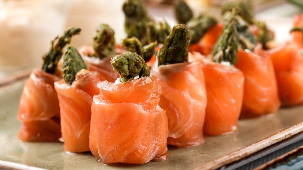 Frontal: Ein Tablett mit mehreren Spargel-Lachs-Röllchen.