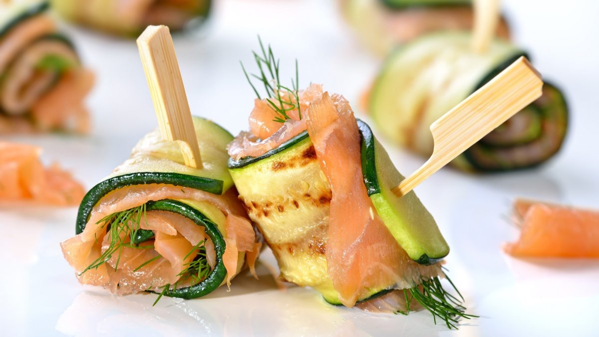 Frontalsicht: Zucchini-Lachs-Röllchen auf einem weißen Untergrund.