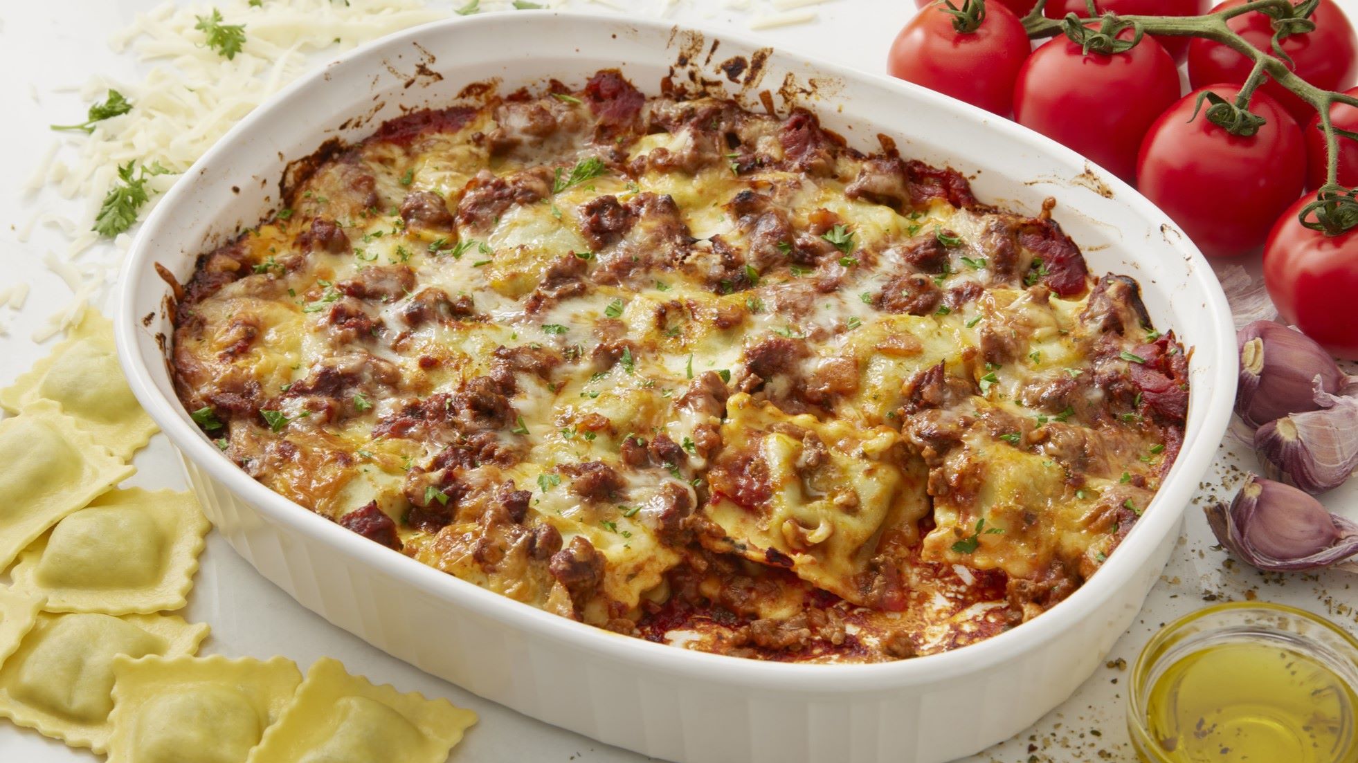Überbackener Ravioli-Auflauf mit Hackfleisch und Käse in einer weißen Auflaufform, dekoriert mit frischer Petersilie.