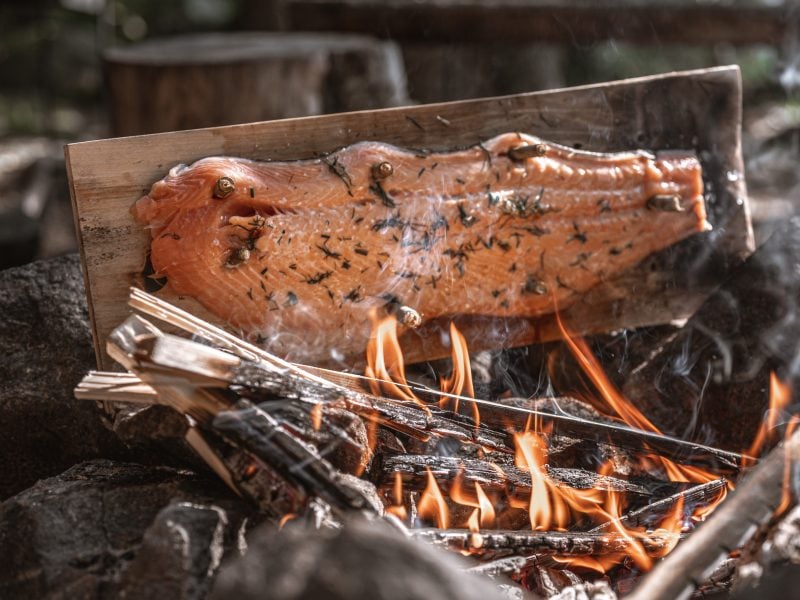 Ein Brett mit Flammlachs am offenen Feuer stehend.