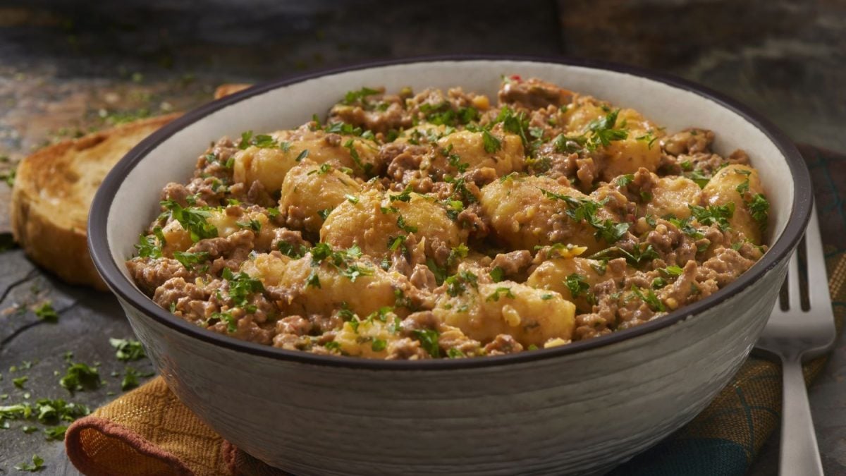 Schüssel mit cremiger Gnocchi-Hackfleisch-Pfanne, garniert mit frischer Petersilie, im Vordergrund ein Stück Brot