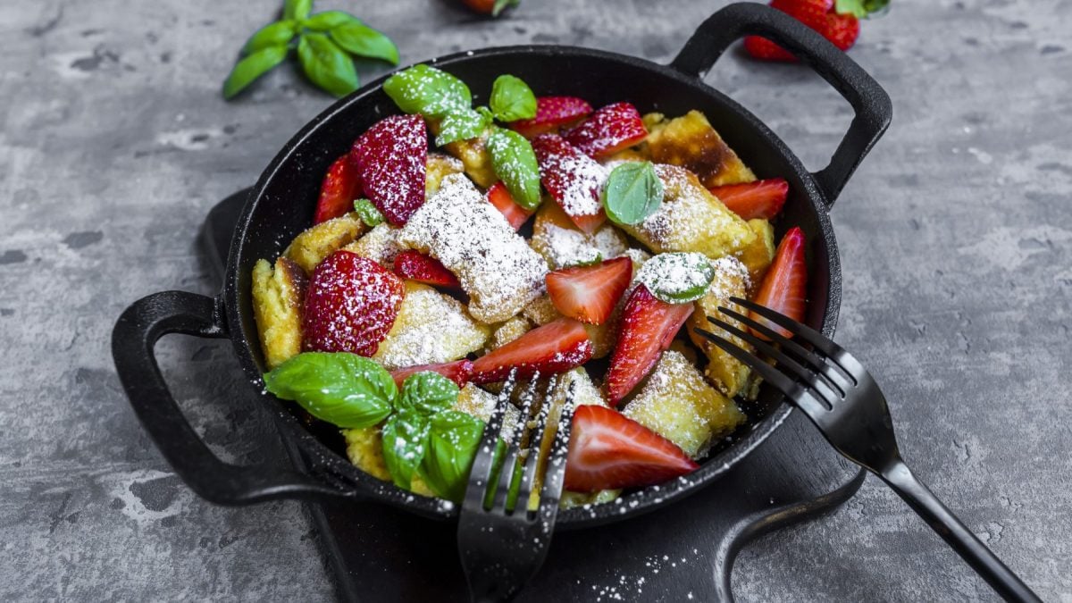 Kaiserschmarrn mit Erdbeeren in einer schwarzen Pfanne auf grauem Hintergrund.