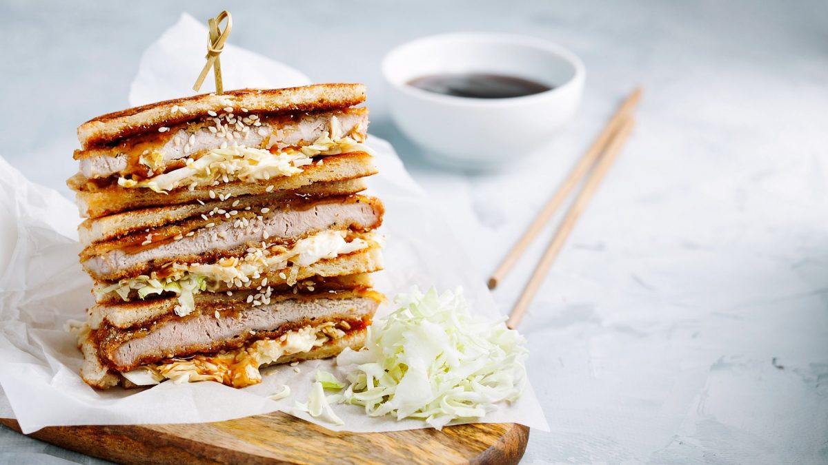 Das angeschnittene Sandwich auf einem Holzbrett und hellem Unter- und Hintergrund. Nah und von der Seite fotografiert.