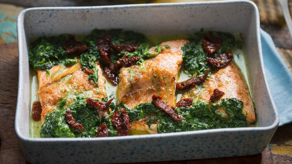 Lachs-Spinat-Auflauf in einer grauen Auflaufform auf braunem Hintergrund.