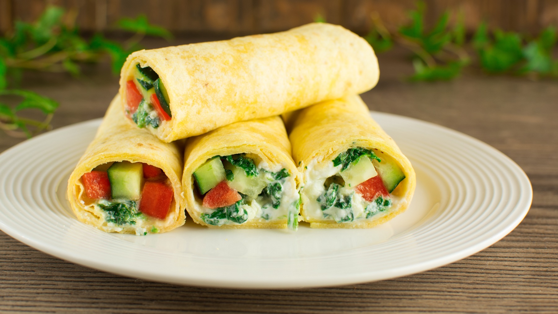 Mehrere Low-Carb-Wraps auf einem weißen Teller und dunklem Holztisch von der Seite fotografiert.