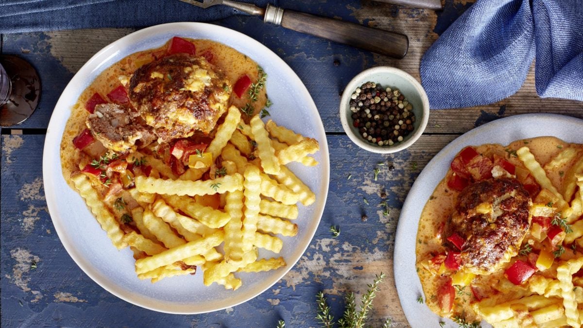 Zwei Teller Mini-Braten in Paprika-Rahm auf hölzernem Hintergrund. In der Mitte ein Schälchen mit Pfefferkörnern und darunter Thymian verteilt.