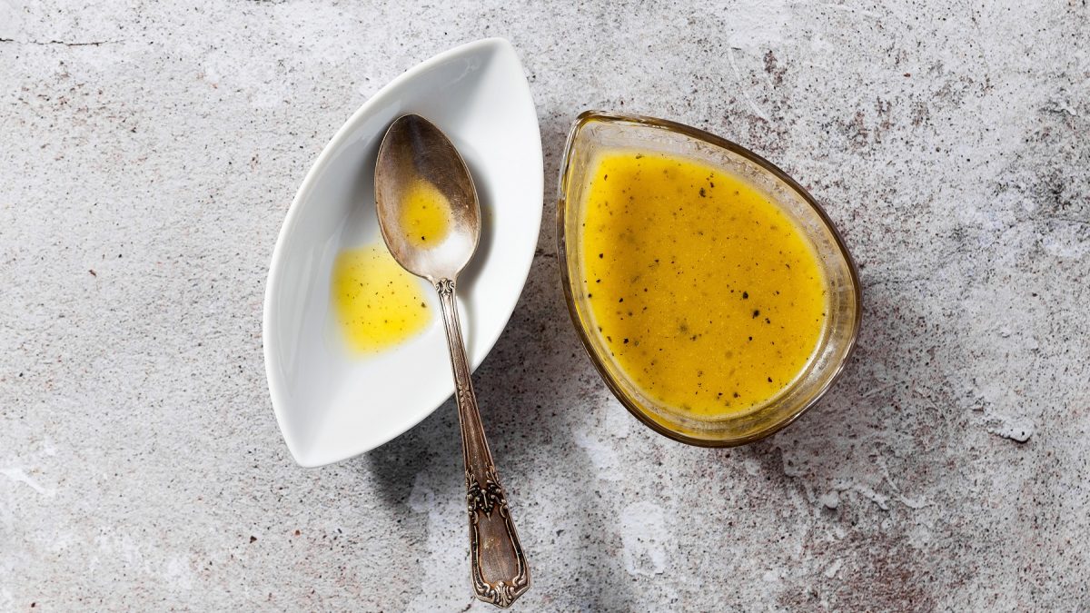 Die Orangen-Senf-Sauce auf grauem Untergrund direkt von oben fotografiert.