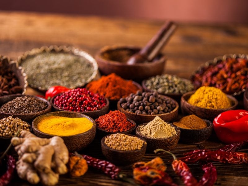 Liste für orientalische Gewürze. Verschiedene Gewürze in Tongefäßen auf dunklem Holztisch. Alles in der Frontalansicht.