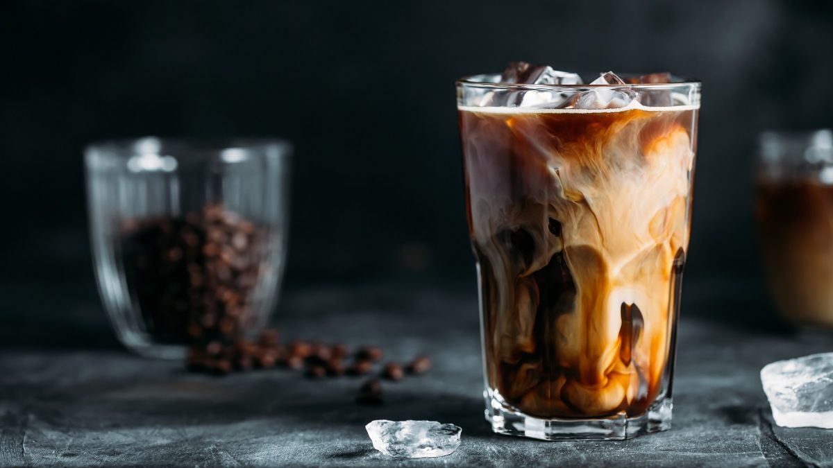 Proffee in einem Glas vor dunklem Hintergrund, wo ein Glas mit Kaffeebohnen steht.