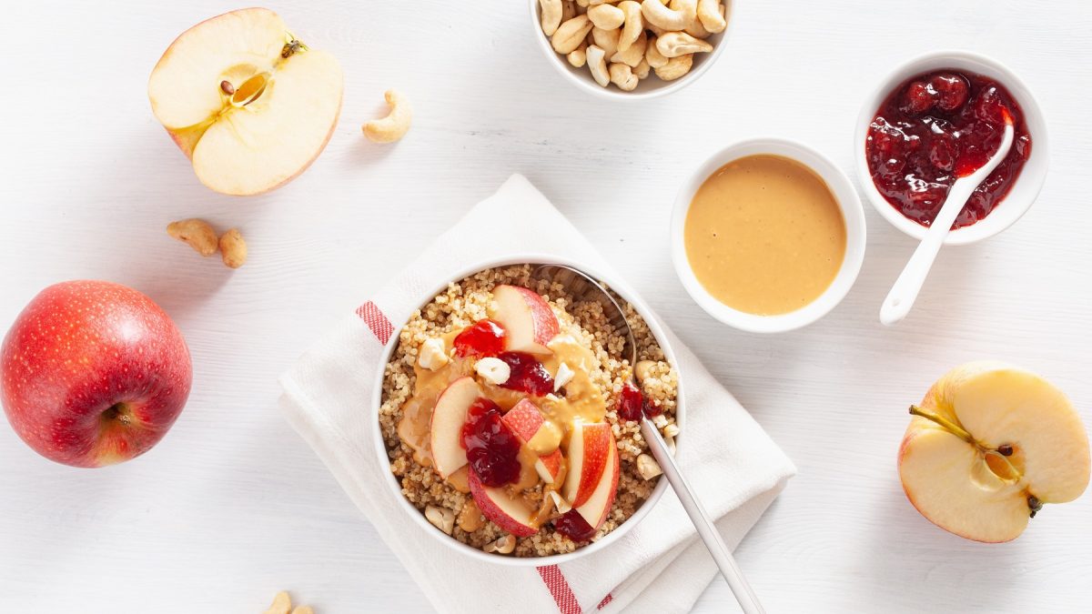 Quinoa Porridge von oben daneben, halbierter Apfel, Schale mit Erdnussmus und Marmelade.