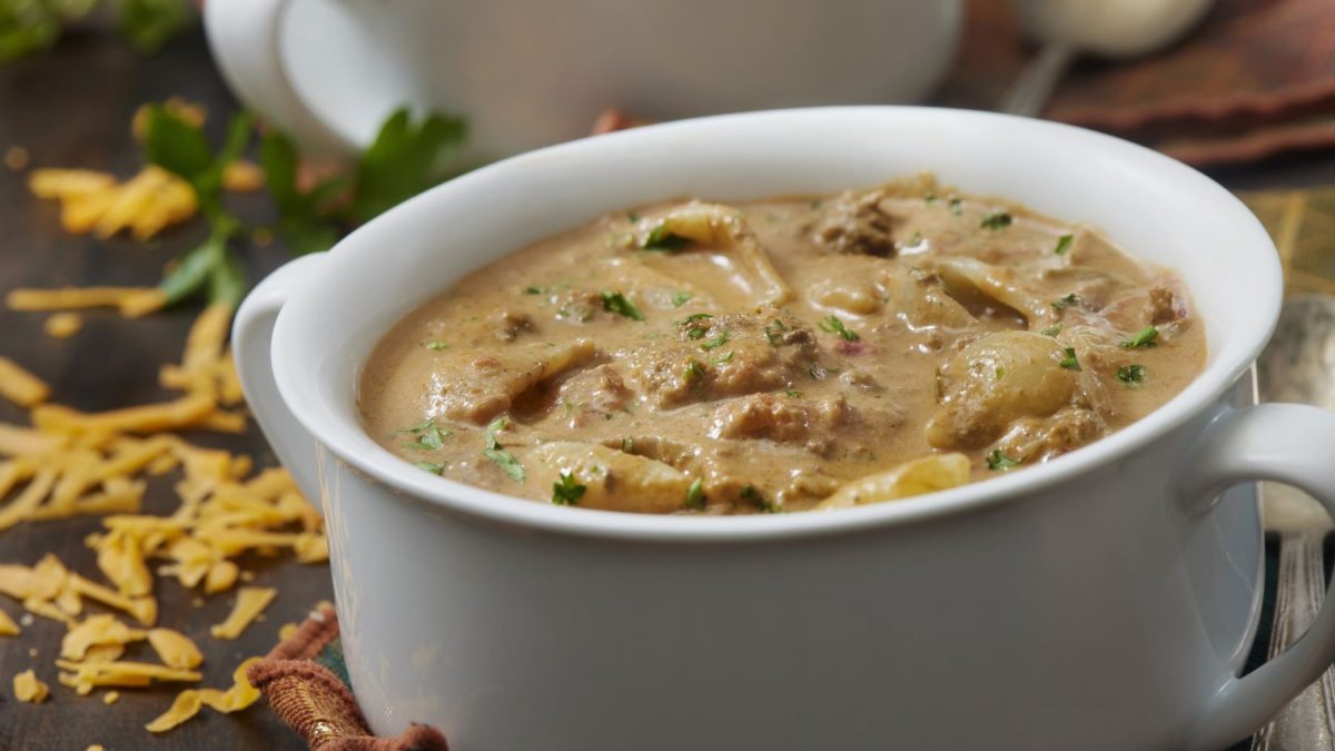 Weiße Schale mit cremigem Hackfleisch-Eintopf, dekoriert mit Petersilie, im Hintergrund geriebener Käse.