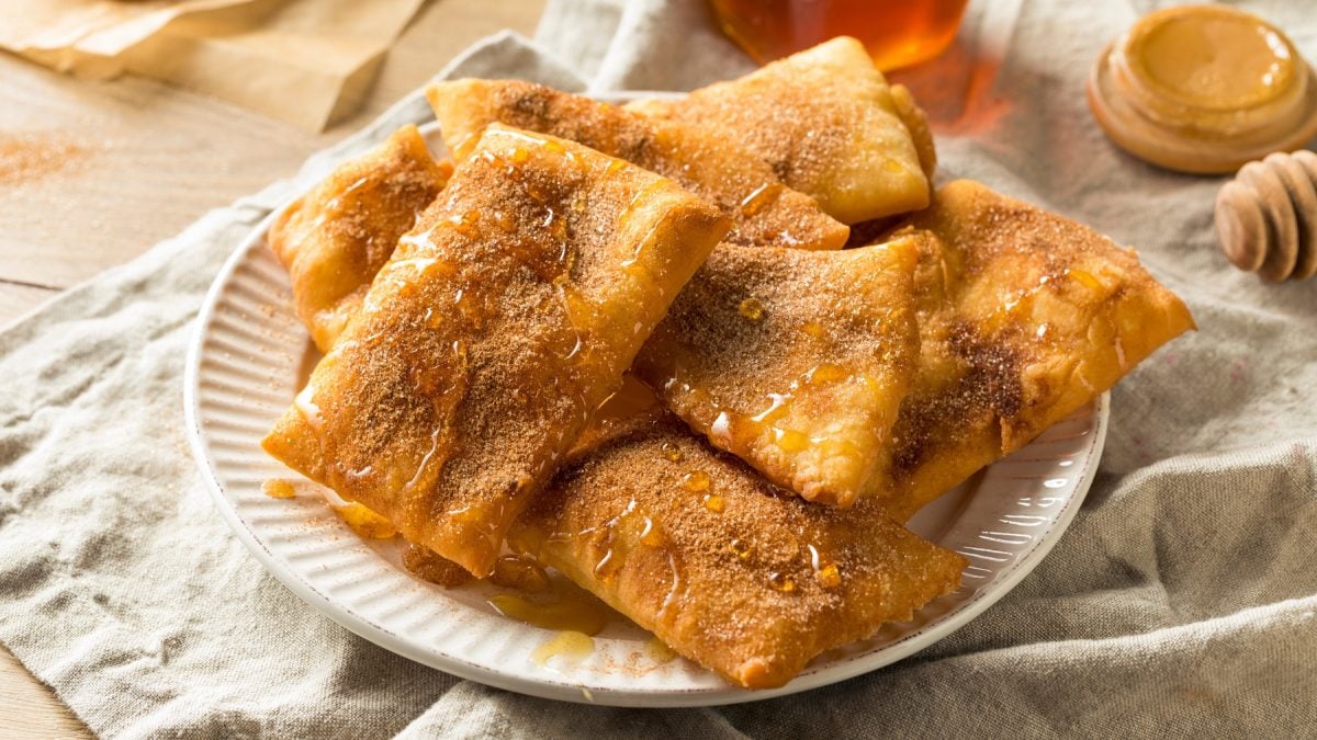 Sopapillas mit Zimt, Zucker und Honig auf einem Teller.