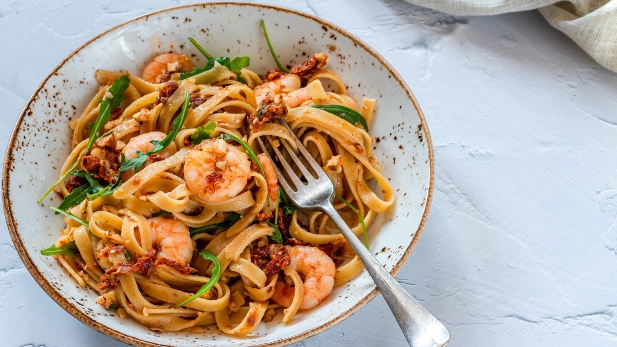 Ein heller, tiefer Teller mit der Pasta auf einem grauen Steintisch und einer Gabel. Alles von leicht schräg oben fotografiert.