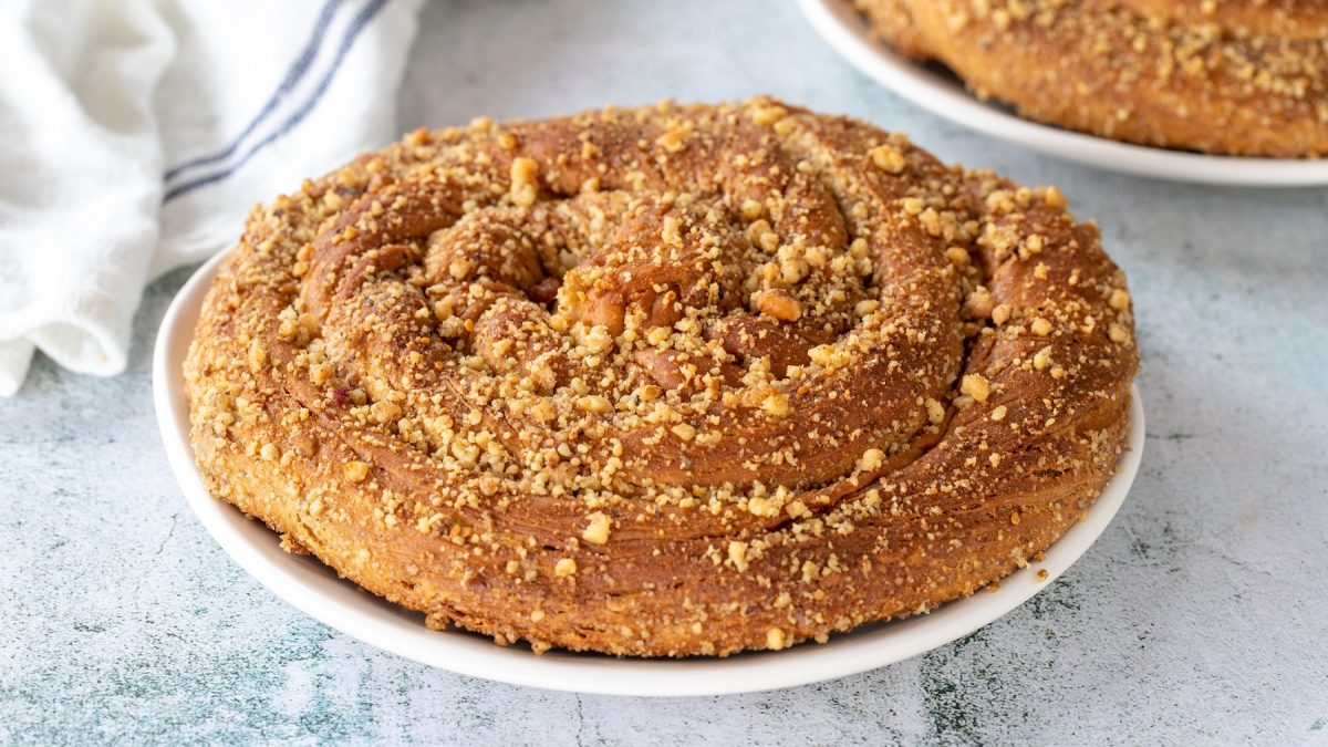 Goldbraune, knusprige Tahinli çörek auf einem weißen Teller, daneben ein weißes Leinentuch auf hellem Hintergrund.