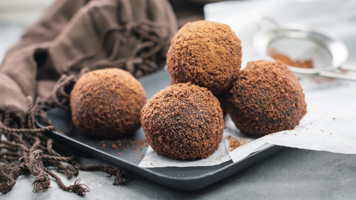 Ein grauer Teller mit einigen Tiramisu-Balls auf grauem Untergrund und mit einer braunen Tischdecke.