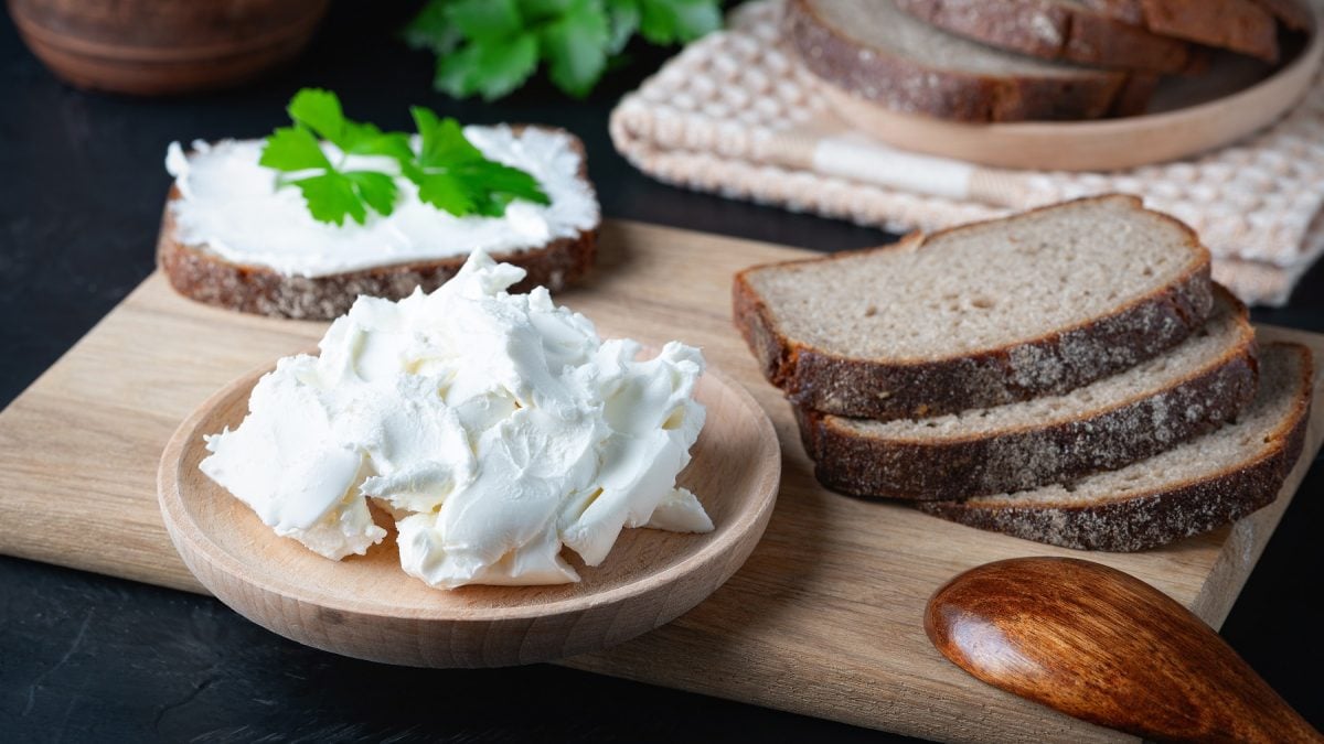 Veganer Quark auf einem Schälchen neben Brotscheiben auf einem Holzbrett.