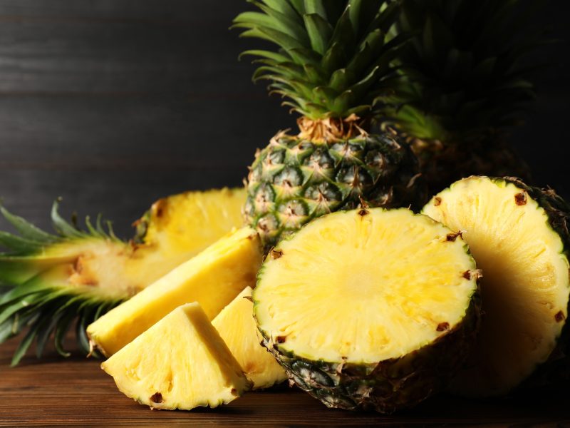 Frontal: Ein Holzbrett mit mehreren Teilen einer angeschnittenen Ananas.