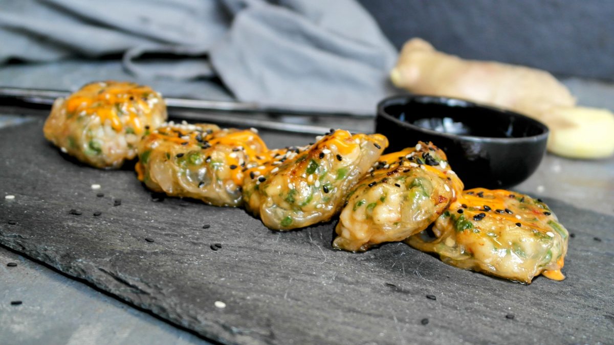 Das Fingerfood mit Garnelen auf einer schwarzen Schieferplatte und grauem Hintergrund. Alles von der Seite fotografiert.