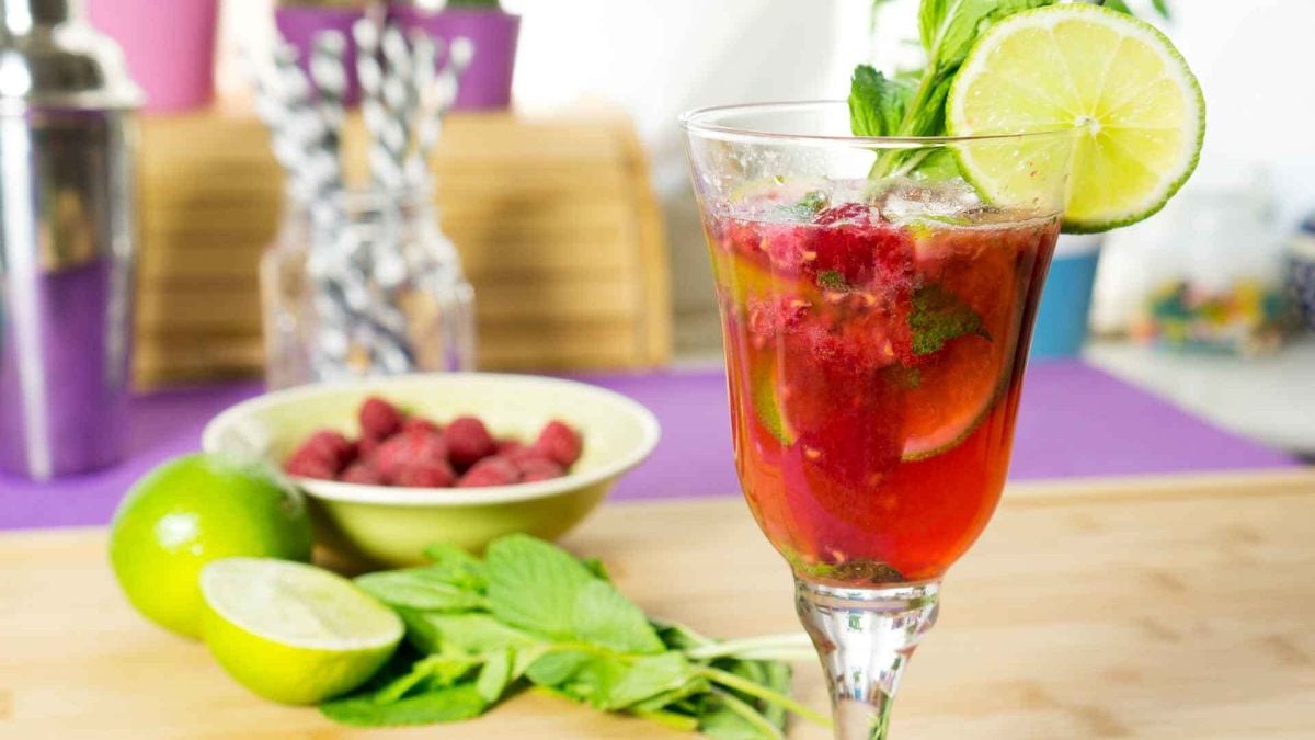 Ein Glas mit dem Himbeer Mojito vor farbenfrohem Hintergrund.
