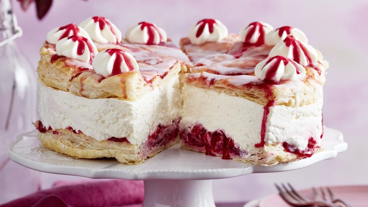 Holländer-Kirschtorte auf einem weißen Tortenteller auf rosa Hintergrund.