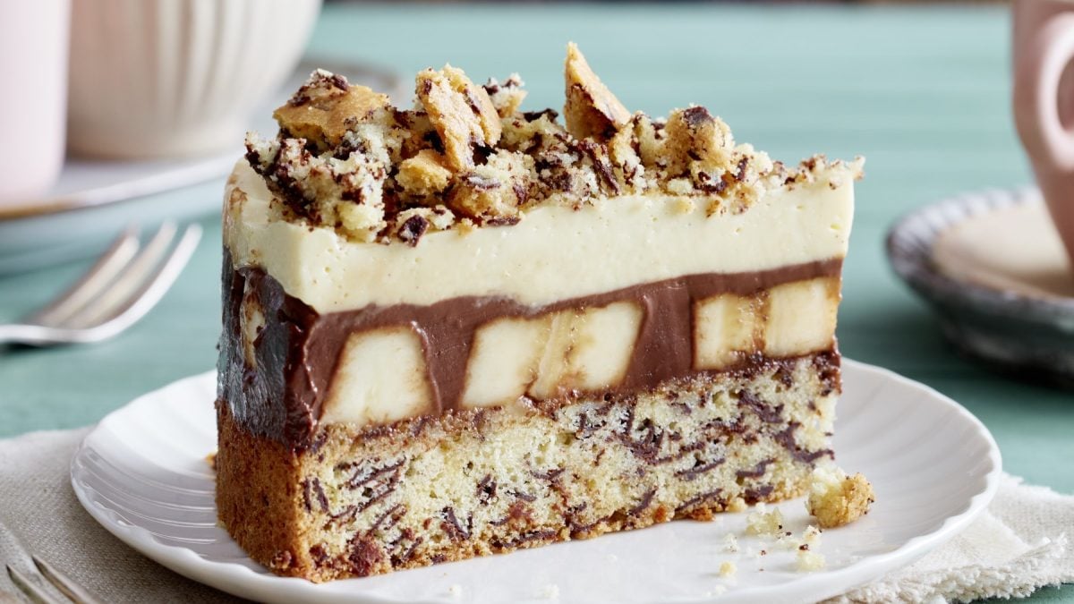 Ein Stück Schoko-Bananen-Torte auf einem weißen Teller auf grünem Hintergrund.