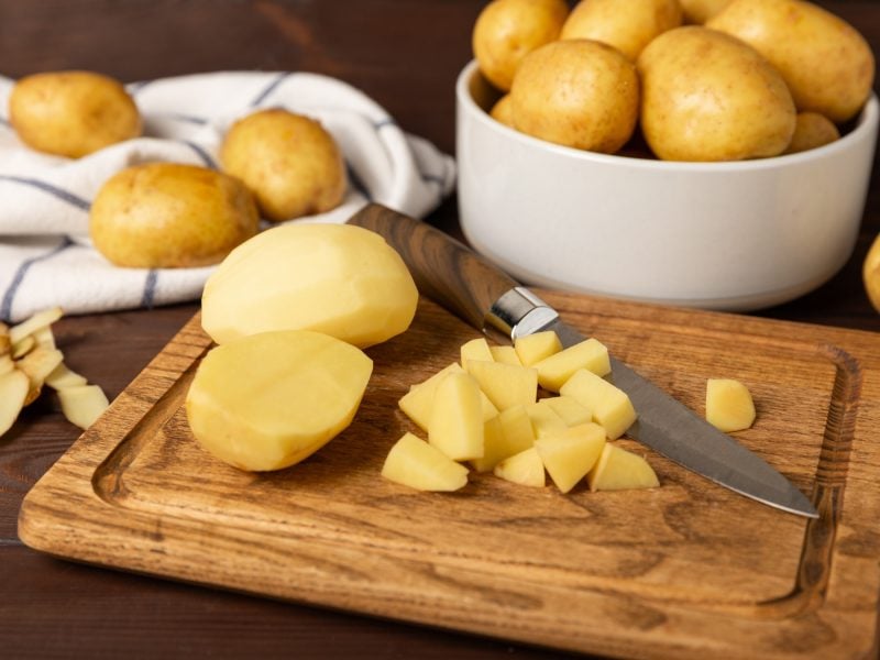 Ungeschälte und geschälte Kartoffeln in Schüsseln und auf einem Holzbrett / Frontal