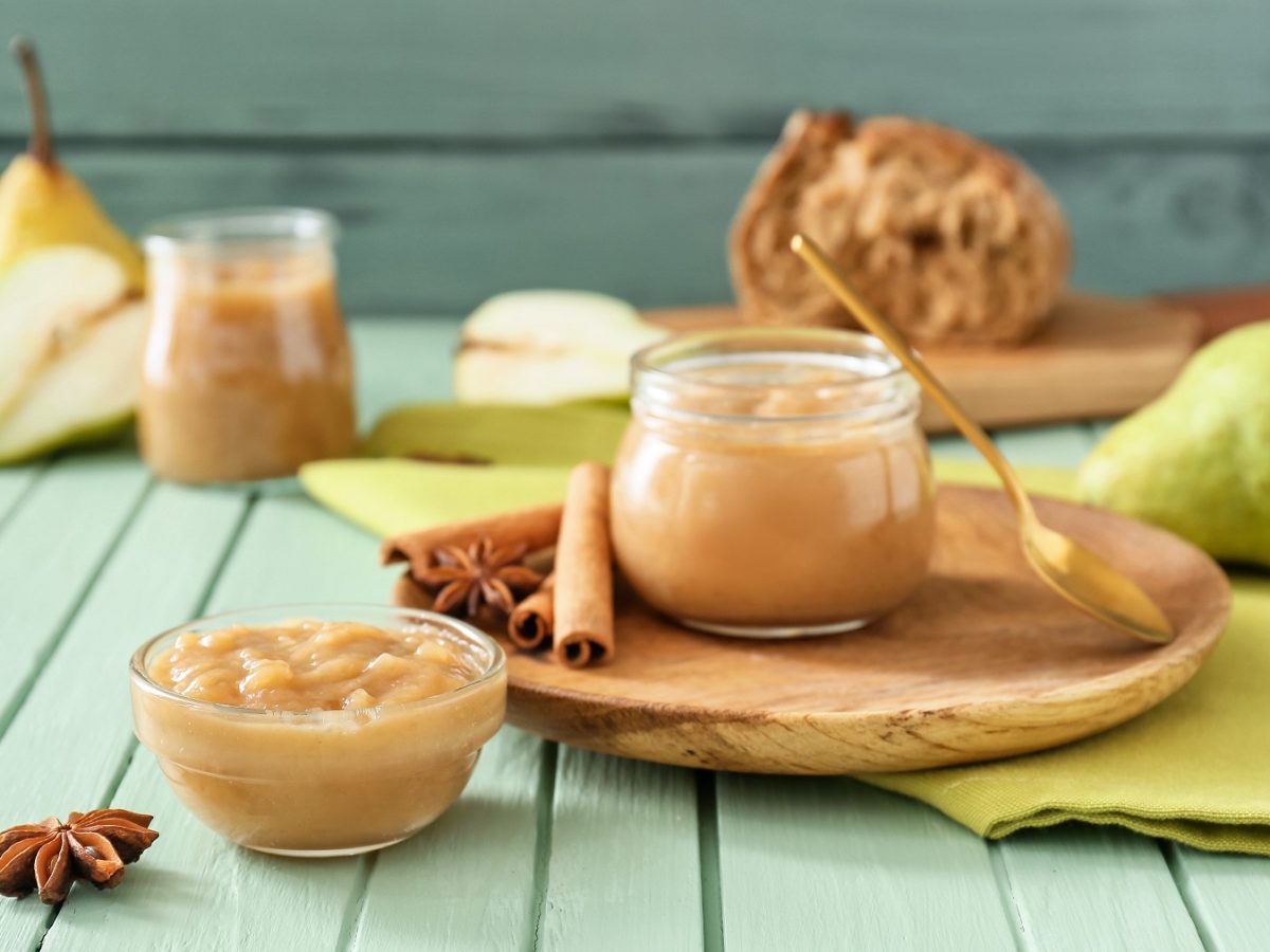 Birnenmarmelade in Schalen auf grünem Tisch, dekoriert mit Zimtstangen, Anissternen und frischen Birnen im Hintergrund.